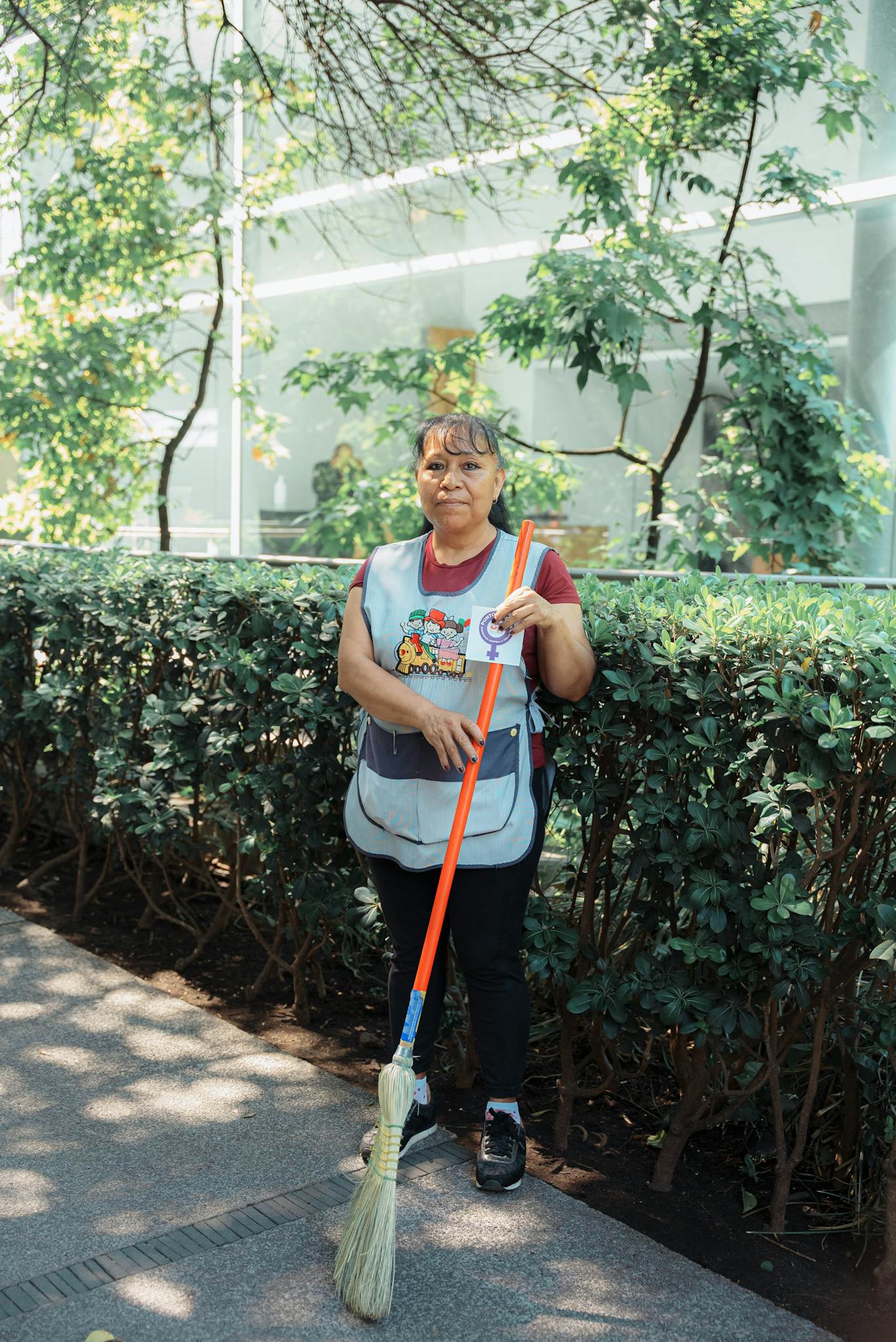 A female city worker sweeping a sidewalk with a broom in an urban outdoor setting.